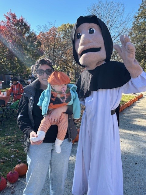Image of woman and baby dressed in pumpkin costume posing with Friar mascot 