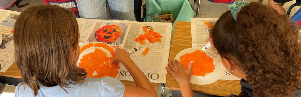 Two children creating pumpkin art using craft materials
